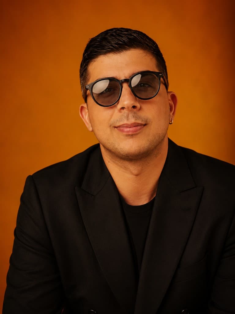 Turuncu arka planda siyah blazer ve gözlükle hazırlanan yapay zekâ moda portresi